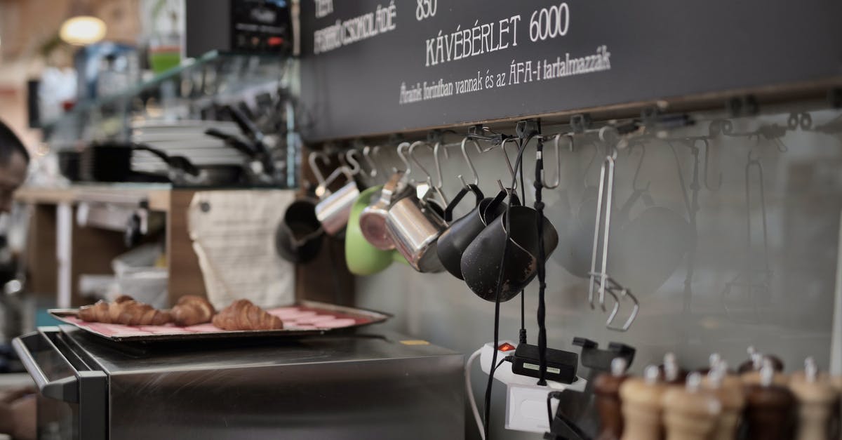 Cook steak in oven with tray meant for deserts? - Various metal cups hanging on hooks near wall above oven with tray with freshly backed croissants in kitchen of modern cafe