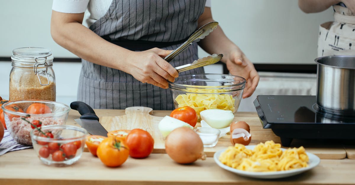 Cooked food / heat and serve meal, long term packaging - Faceless women in aprons cooking delicious pasta with fresh tomatoes standing at counter in modern kitchen