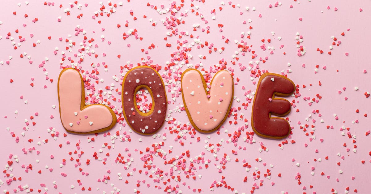 Cookie Biscuits: What happened? - Top view of composed cookies making Love inscription with small heart shaped confetti on pink background