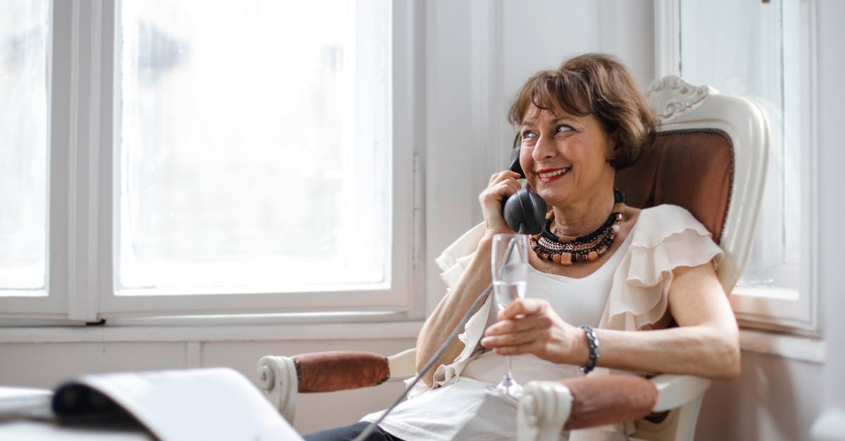 Cooking away alcohol - Cheerful relaxed female in casual clothes with wineglass of drink looking away and smiling while sitting in vintage armchair and talking on retro phone on light balcony of modern apartment