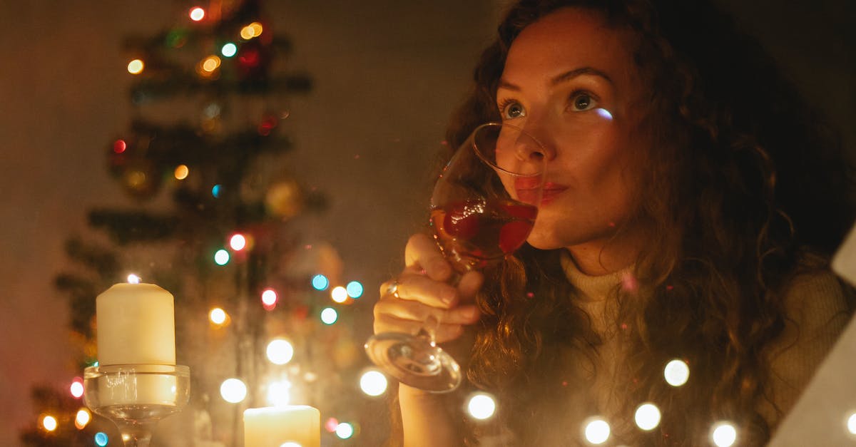 Cooking away alcohol - Through glass of dreamy female with glass of champagne sitting among shiny garlands and burning candles during Christmas celebration