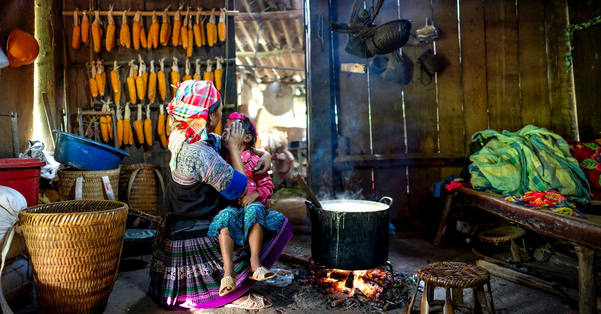 Cooking dried corn - Ethnic mother with unrecognizable daughter stirring food in cauldron indoors