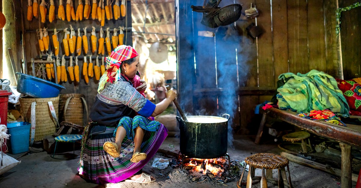 Cooking dried corn - Anonymous ethnic mom touching face of girl while looking at each other against cauldron on fire at home