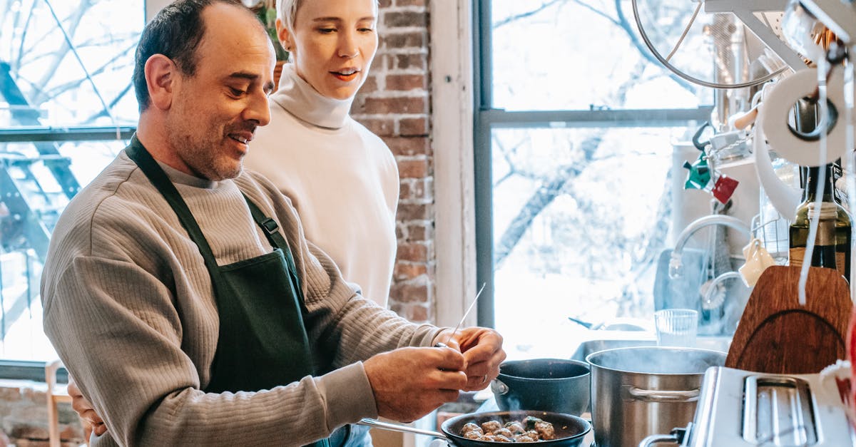 Cooking meat directly above the flame of a gas stove - Smiling man in apron cooking against attentive girlfriend and gas stove with meatballs in pan at home