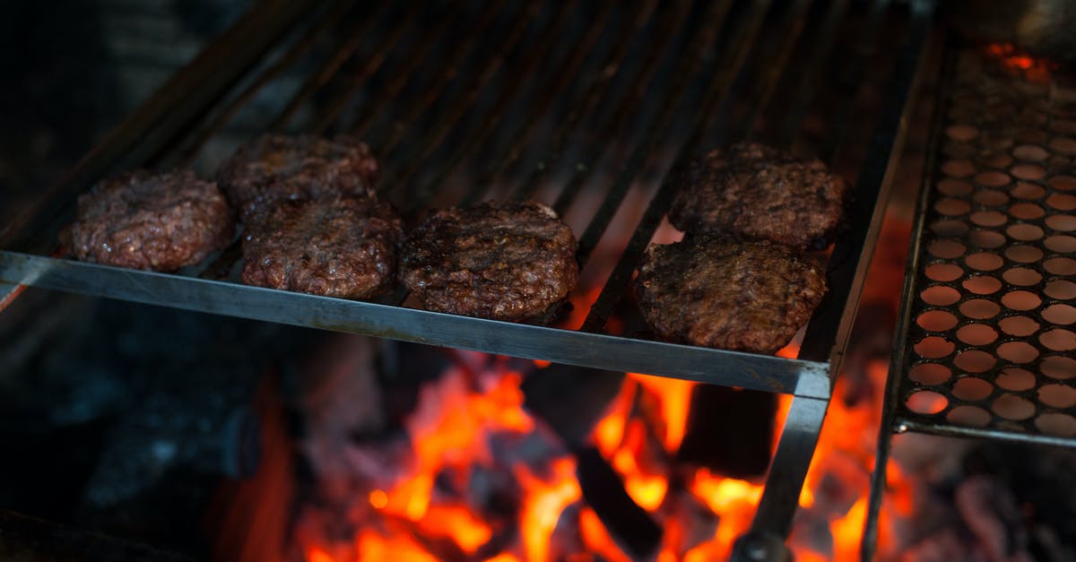 Cooking meat directly above the flame of a gas stove - From above of appetizing meat patties grilling on metal barbecue grade above fire in kitchen