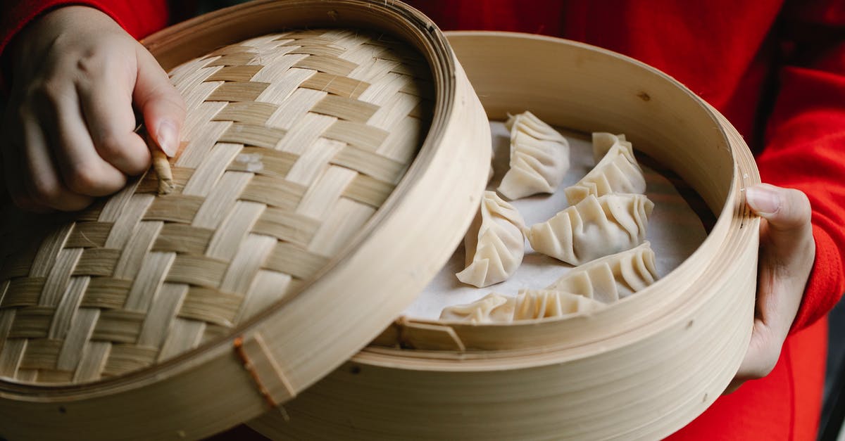 Cooking messy foods in a bamboo steamer without a cleaning nightmare - Crop anonymous cook in red clothes opening bamboo steamer with raw delicious dumplings