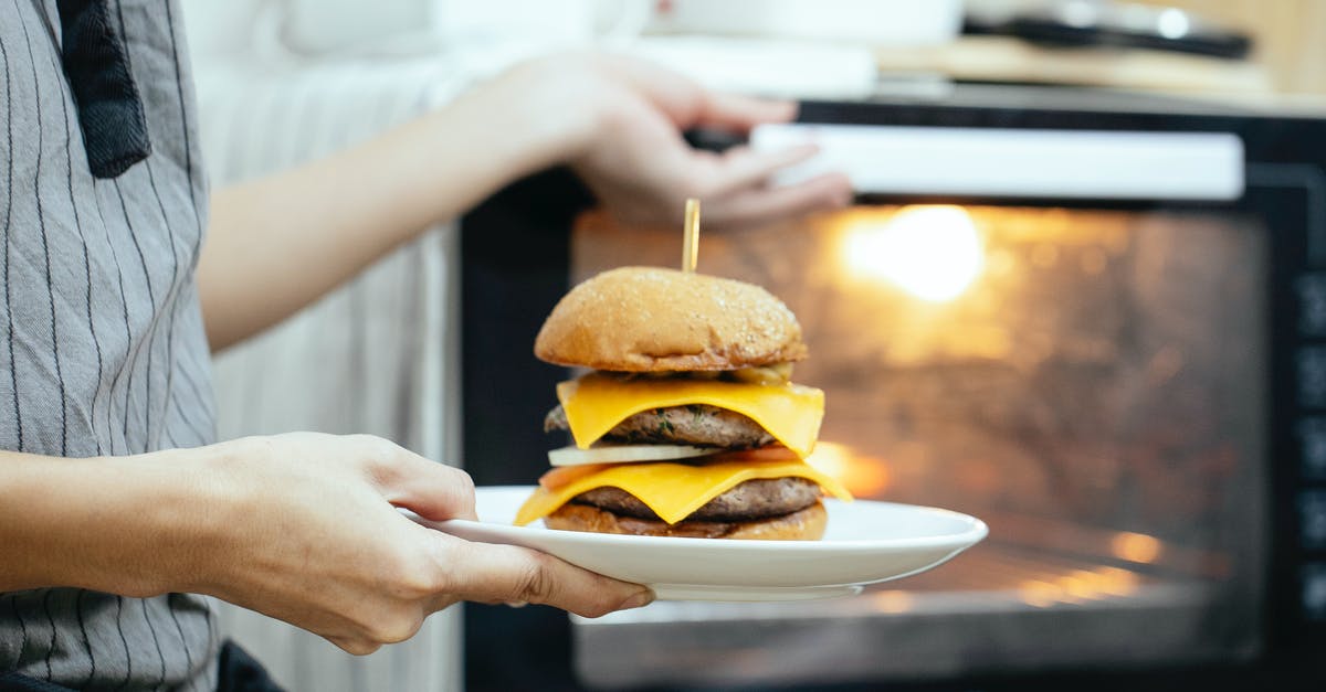 Cooking over an open flame at home - Unrecognizable person with plate of burger in hand opening door of oven to roast food while cooking in kitchen on blurred background