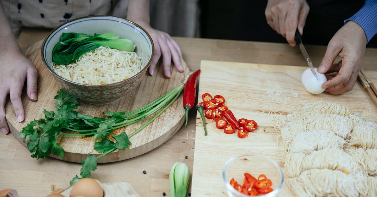 Cooking pasta in a Pressure Cooker - From above anonymous females cutting boiled eggs on wooden cutting board while cooking traditional Asian noodle soup in kitchen