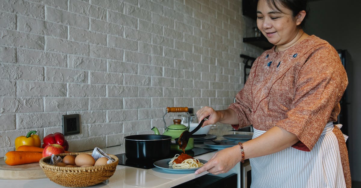 Cooking thick fresh egg pasta - Content senior ethnic woman cooking appetizing spaghetti with sauce standing at table with fresh vegetables and eggs in kitchen