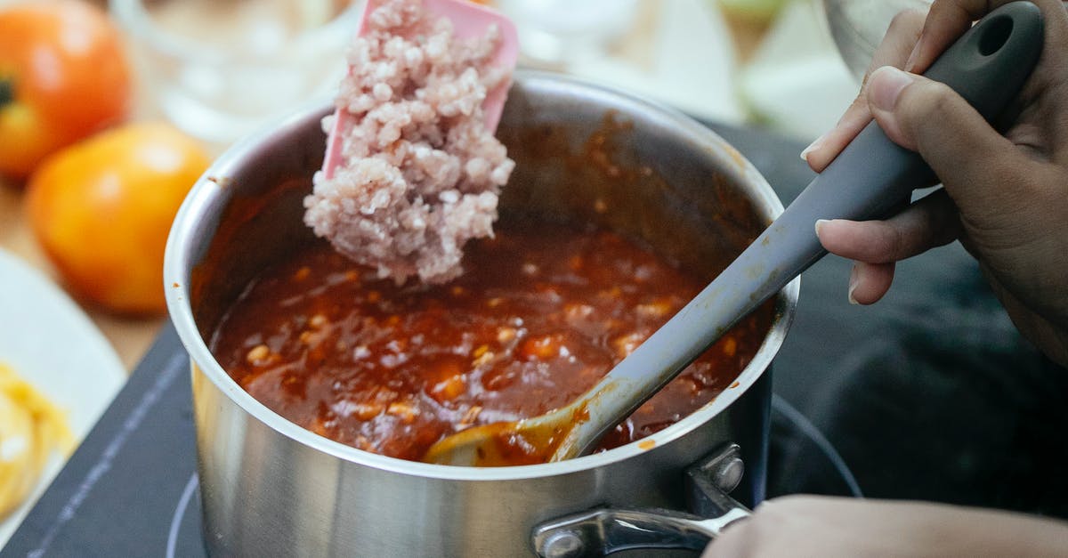 Cooking two pieces of meat in pressure cooker - From above of anonymous cook adding minced meat into pan with boiling chili while standing near stove on blurred background