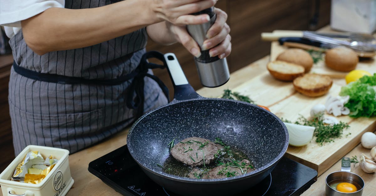 Cooking two pieces of meat in pressure cooker - Unrecognizable female cook wearing apron adding seasoning on cutlets while preparing delicious burger at table with stove in kitchen