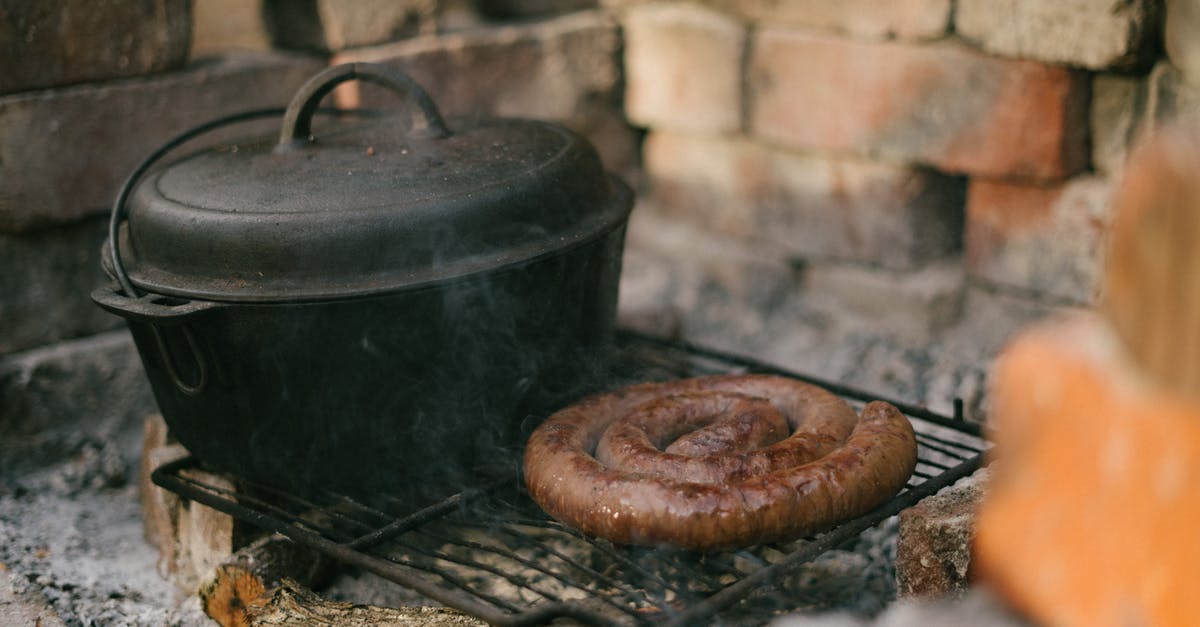 cooking with a round based clay pot on an electric stove - Footlong Sausage And Black Cooking Pot on Black Metal Grill