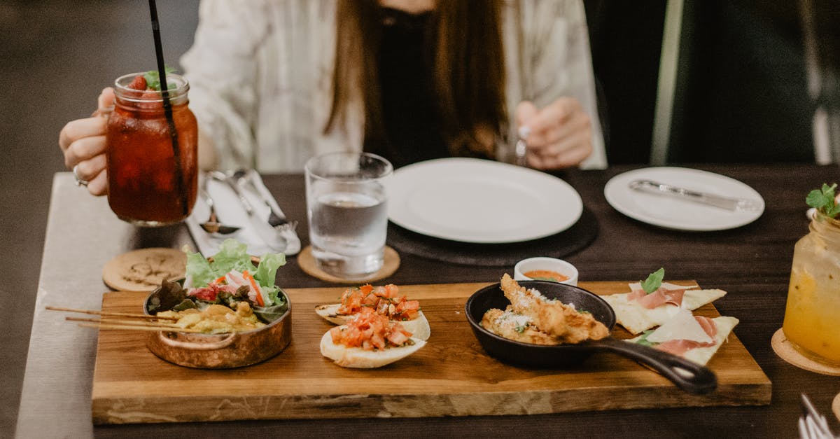 Cooking with sourdough starter - Crop unrecognizable female in casual clothes having dinner in Asian restaurant while sitting at table with berry mocktail and grilled meat on sticks served with tomato sandwiches and spring rolls