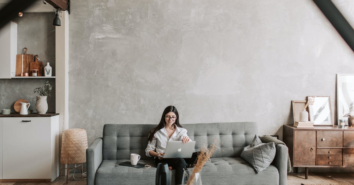 Cooling coffee rapidly without dilution - Happy female remote worker in eyeglasses sitting on cozy sofa with netbook and cup of coffee in loft style room with wooden floor and concrete wall