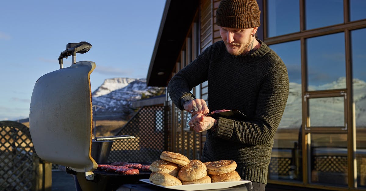 Cooling off a kettle-style grill - Concentrated young male in warm outfit preparing delicious grilled meat while standing against cozy house in winter day