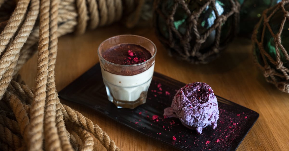 Coriander in a blueberry ice-cream? - From above of glass of appetizing cream dessert with chocolate top served with blueberry ice cream garnished with pink dye on ceramic plate surrounded by rope tied in knot and dark green glass balls in grid