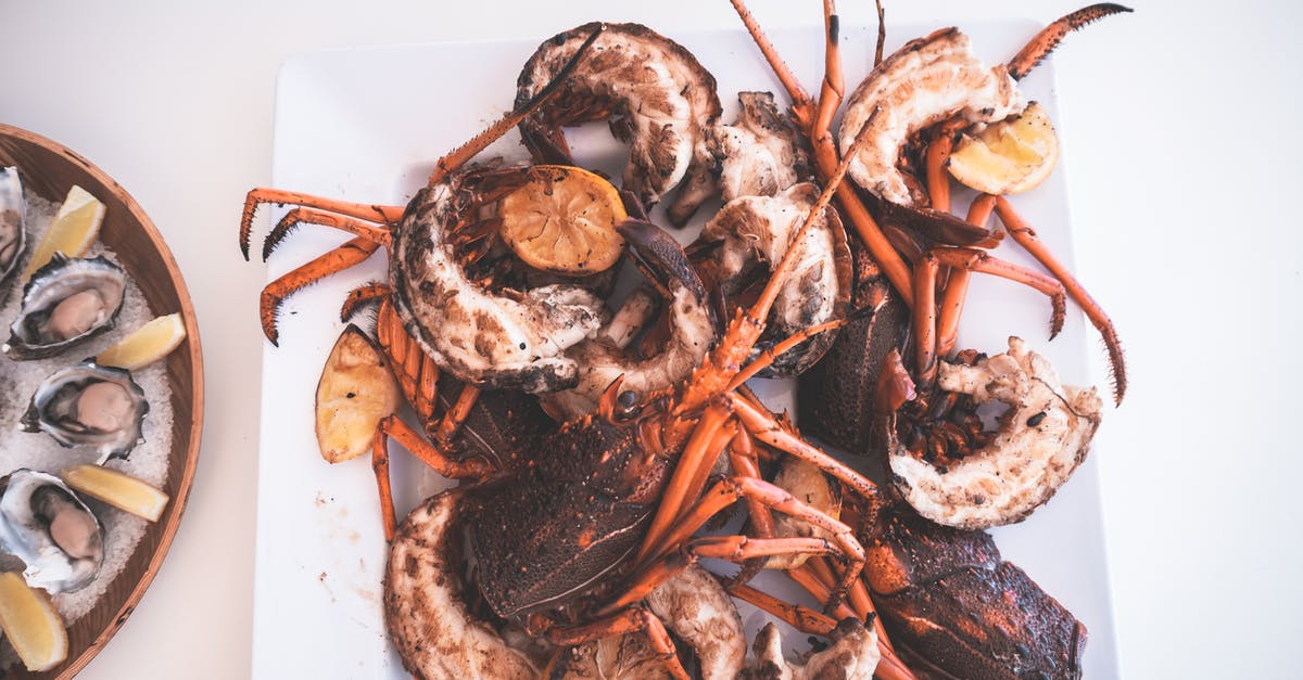 Could I possibly tell imitation lobster from real lobster? - Top view of appetizing grilled lobsters with lemons served on white table near tray of oysters in restaurant