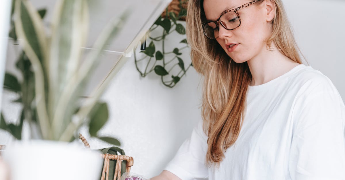 Couldn't make pesto in a blender - Low angle of focused female in eyeglasses and home t shirt standing at counter with green potted plants while cooking lunch snack at home