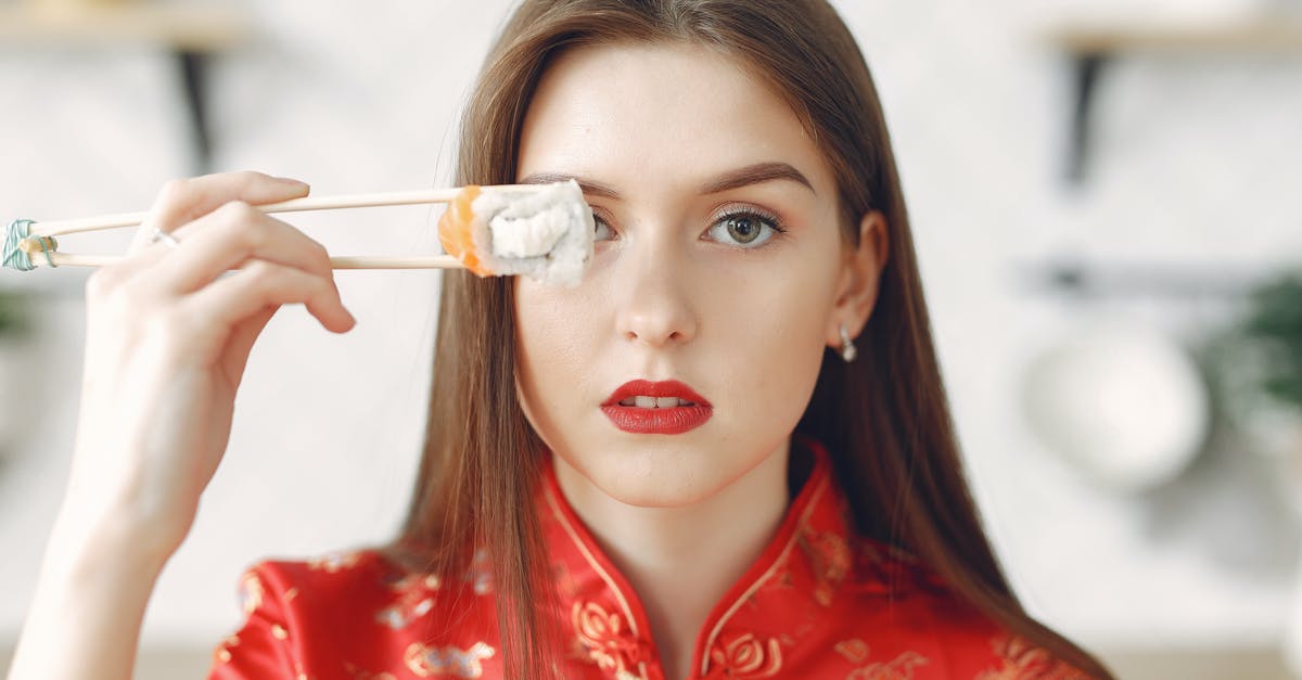 Cracked Mexican/Spanish style rice - Young lady with dark hair in stylish wear holding chopsticks with sushi and covering eye while resting in light kitchen at home