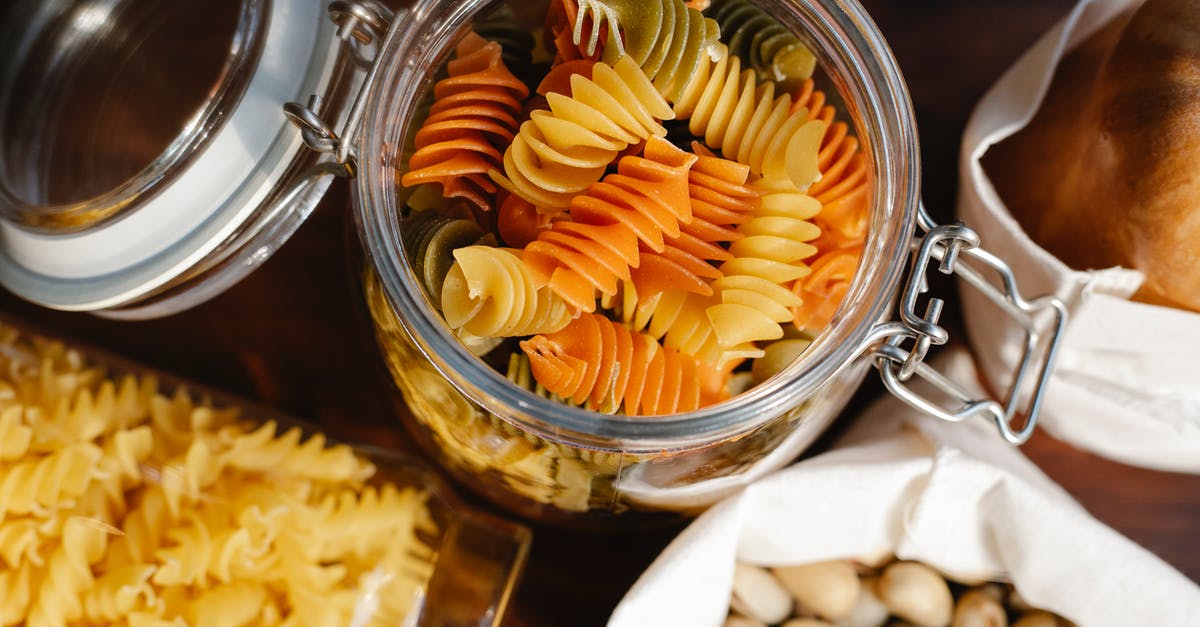 Cracking open a pistachio - From above glass jar with colorful rotini placed on table near fusilli in container and pistachios and bread in bags