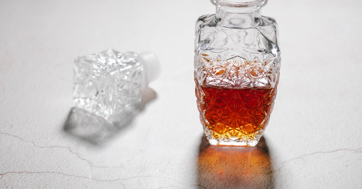 Cracking open a pistachio - From above of open crystal glass jug with alcoholic beverage placed on white table with cracks