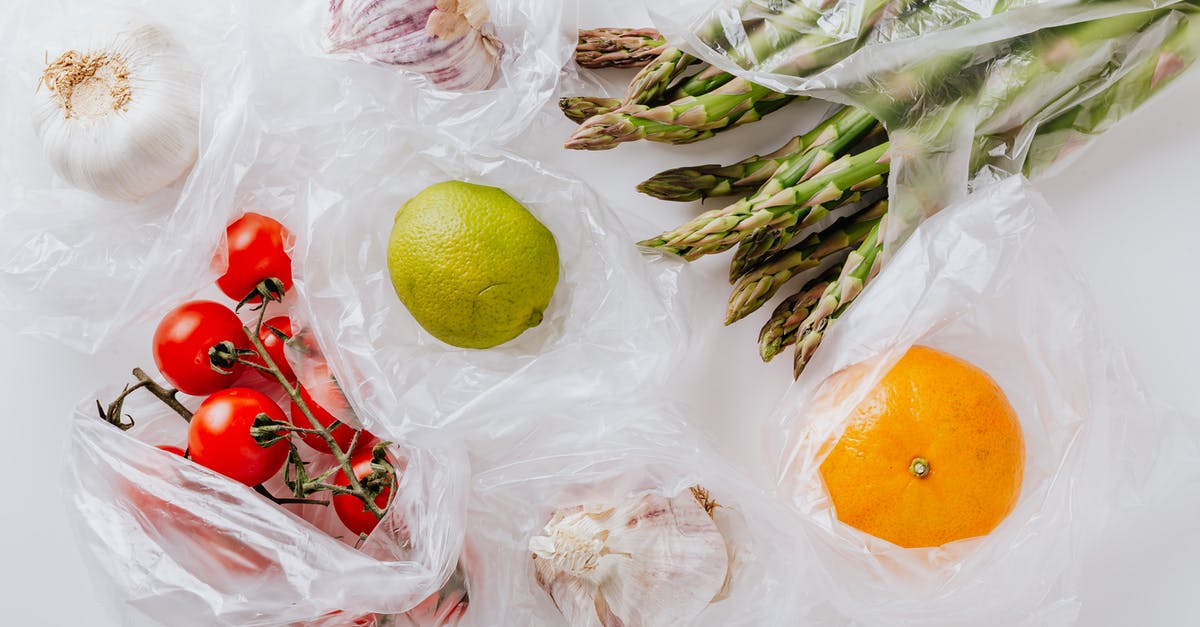 Cream of Tomato with garlic + cilantro stalks aroma - From above of bunch of tomatoes with raw asparagus put into transparent plastic bags on white table near citrus fruits and garlic bulbs