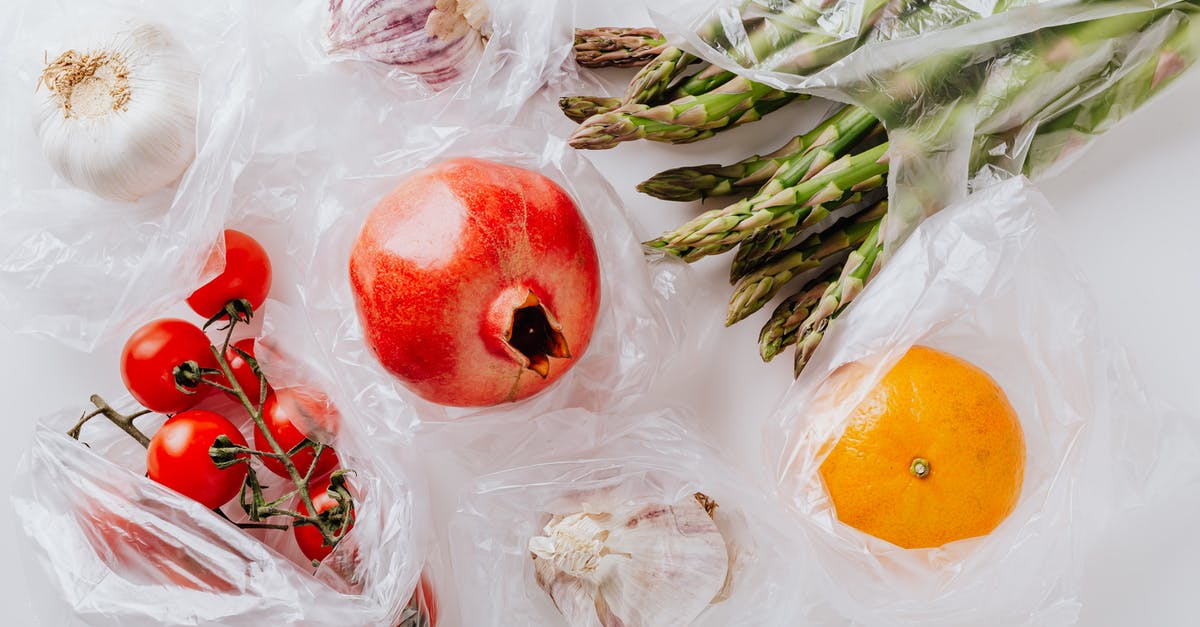 Cream of Tomato with garlic + cilantro stalks aroma - Top view of pomegranate in center surrounded by bundle of raw asparagus with orange and bunch of tomatoes put near heads of garlic in plastic bags on white surface