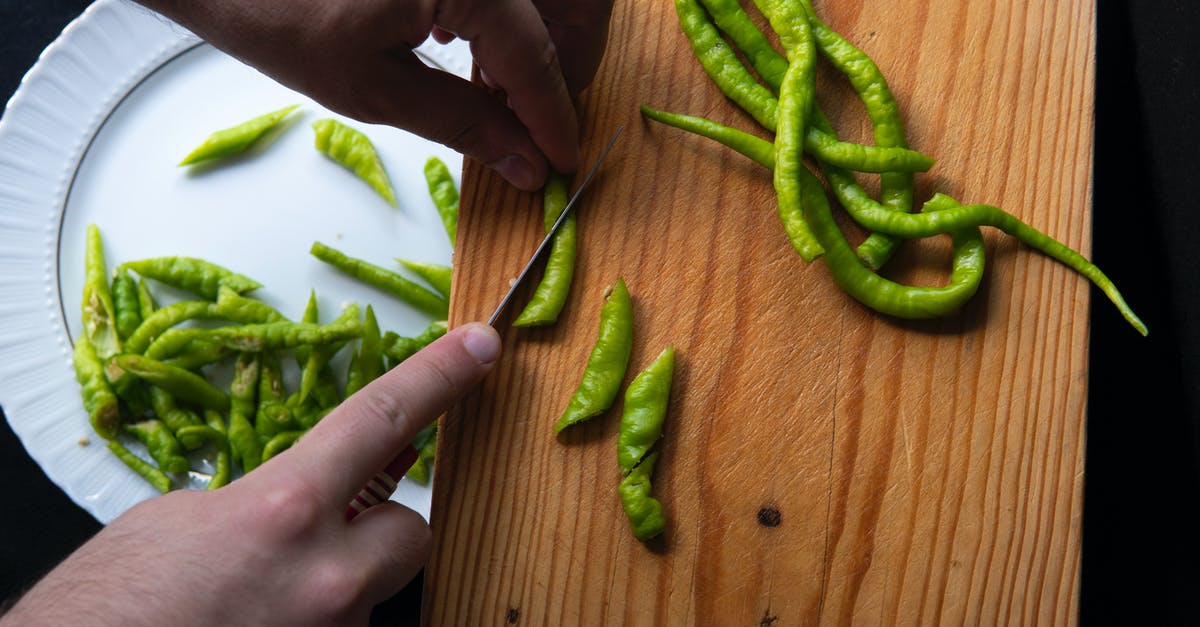 Create hot "sauce" from capsaicin extract - From above hands of crop unrecognizable person cutting hot peppers on cutting board and putting slices on plate