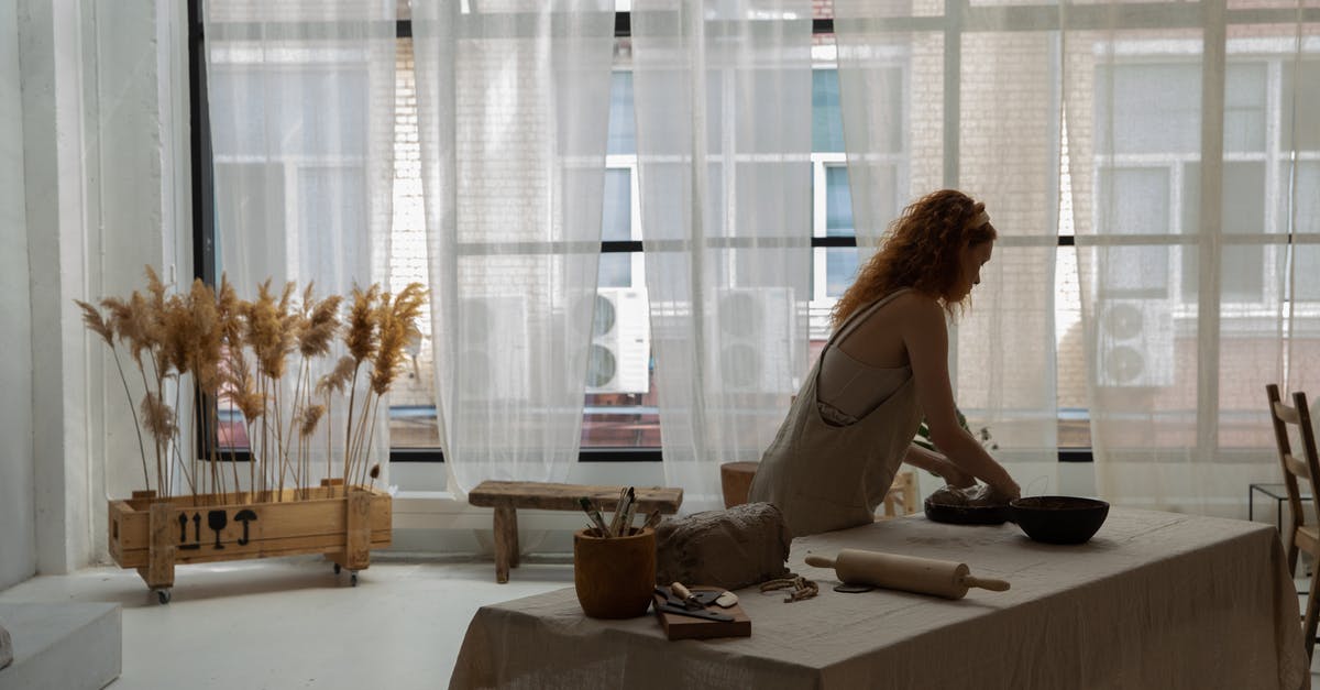 Creating ideal temperature for dough to rise - Side view faceless female wearing apron placing clay slab on baking pan while making earthenware in contemporary studio