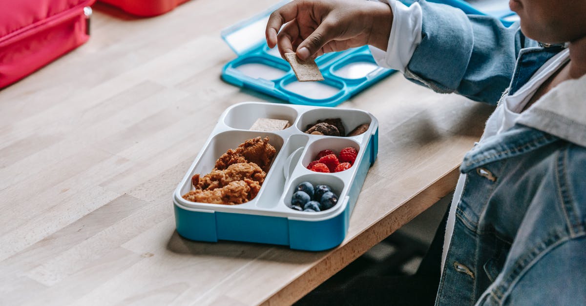 Crispy cold fried chicken - From above side view of crop unrecognizable ethnic schoolkid at table with lunch container full of tasty food