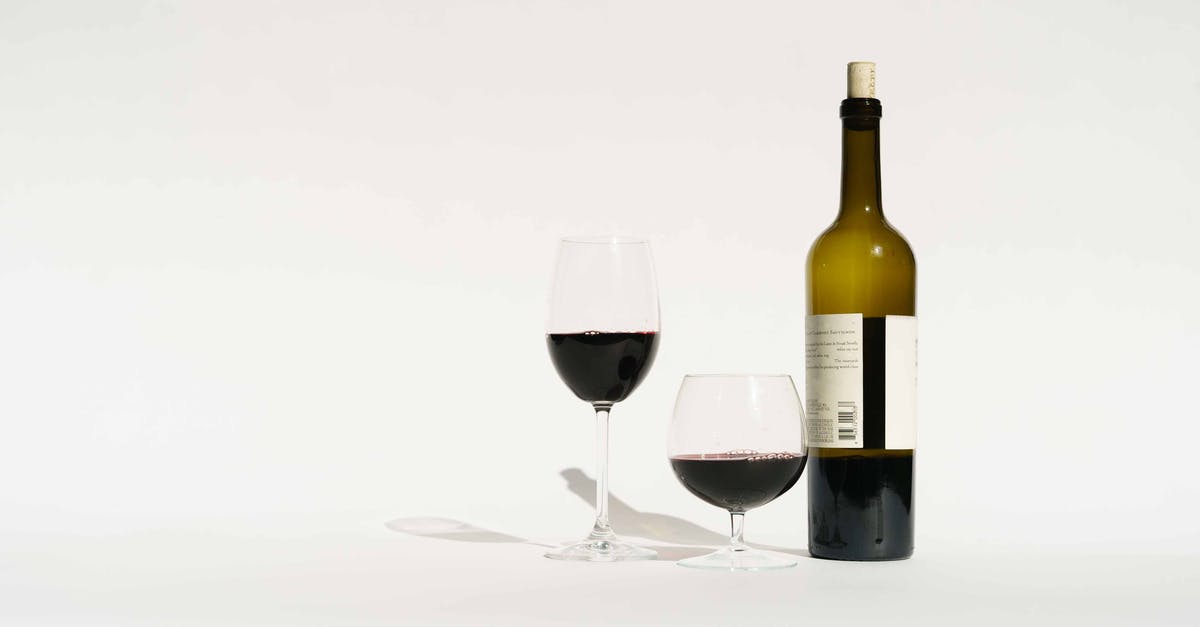 Crystals on bottle of sweet alcohol - Red wine made from dark colored grape varieties in bottle and glasses placed in white studio