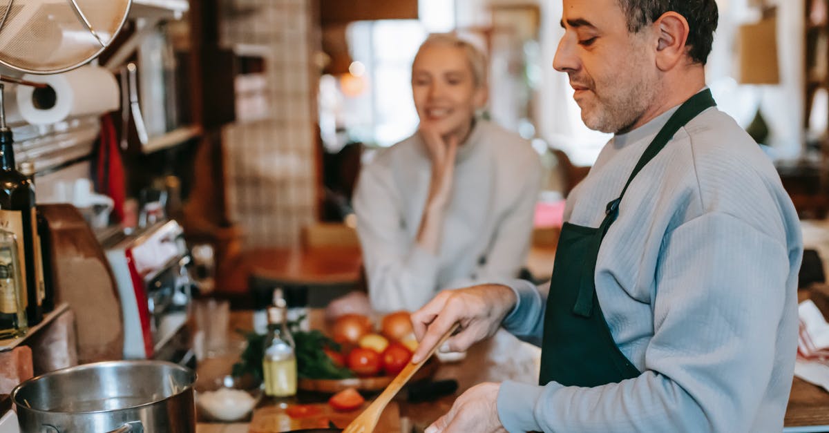 Culinary term for frying in water (without oil)? - Crop male stirring tasty meatballs in pan while preparing lunch against smiling female beloved at home