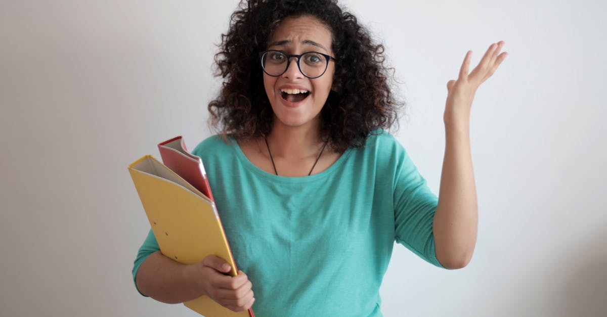 Cupcake Papers Peeling away - Dissatisfied annoyed woman with mouth opened wearing glasses and turquoise blouse looking away and screaming while standing against white wall with folders of documents and having problems in work