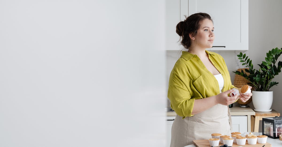 Cupcake Papers Peeling away - Female cook standing near table and looking away while preparing tasty cupcakes in light kitchen