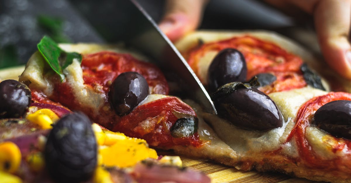 Cut food with fork and sharp knife - metal in food? - Crop anonymous person cutting tasty pizza with cheese tomato and olive on wooden board