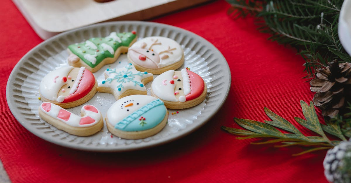 Cutting windows into a premade gingerbread - From above of plate with yummy gingerbread cookies placed on table with Christmas decorations in daytime