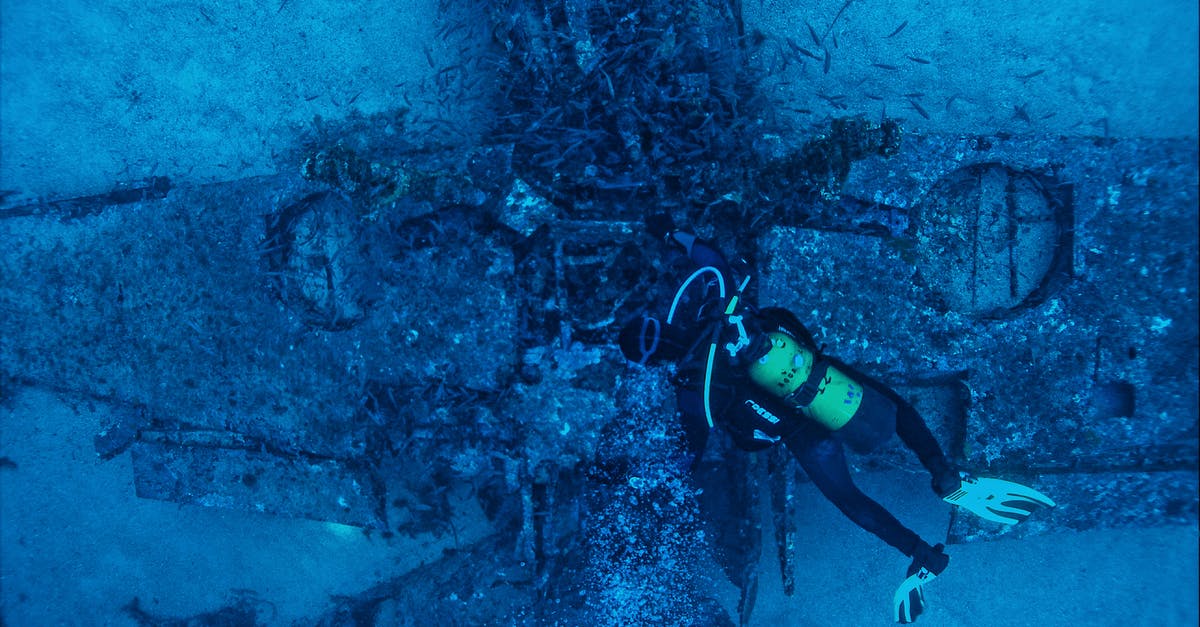 Damage to pan bottom - Top view of unrecognizable person in wetsuit inspecting rough remains of sunken plane on bottom of sea