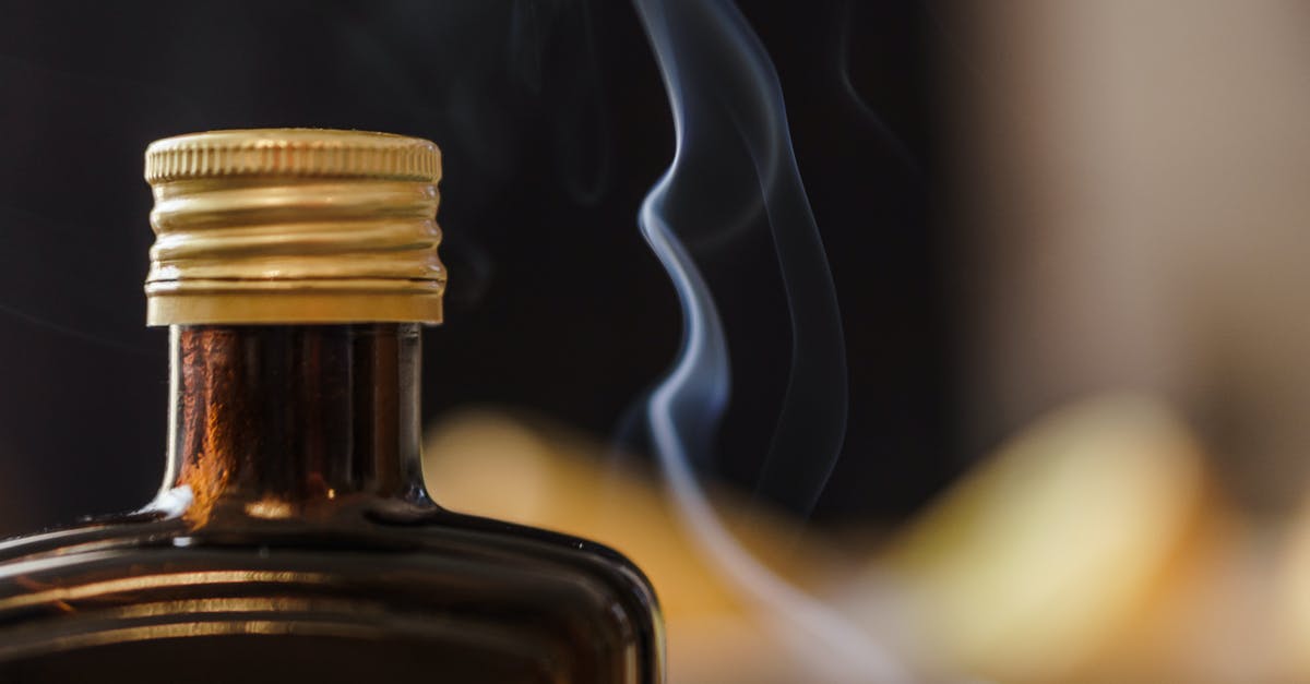 Date cookies are thin and spread out - Shiny bottle of alcohol with opaque glass and ribbed cap near fume in air on blurred background