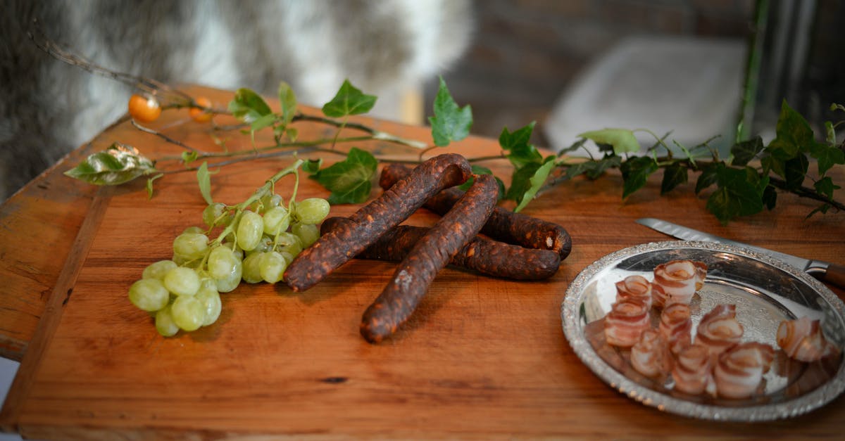 Dealing with a hank of natural sausage casings - From above of appetizing sausages placed near branch of grapes and bacon plate on wooden board