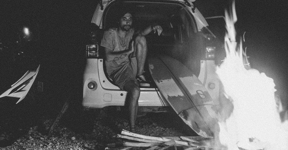 deli ham left in warm car - Black and white bearded young male surfer in summer clothes recreating in SUV car trunk and looking at bonfire at night