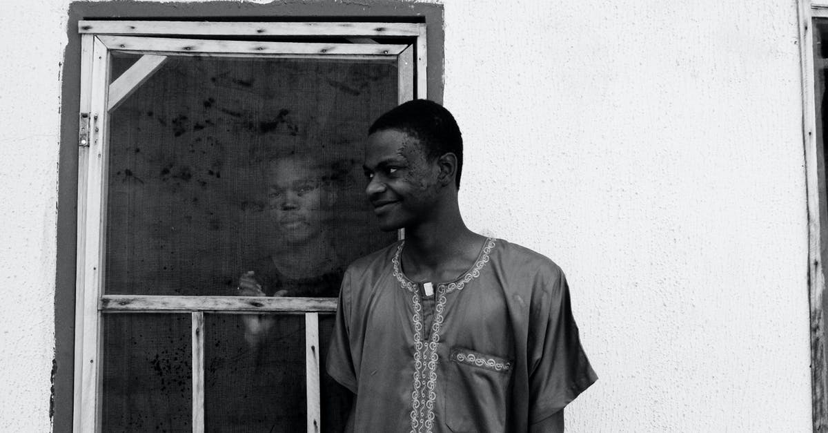 Delicata squash - good outside but not sure about inside - Black and white of slim happy African American guy looking away while standing near house with concrete walls and old window with serious partner inside building