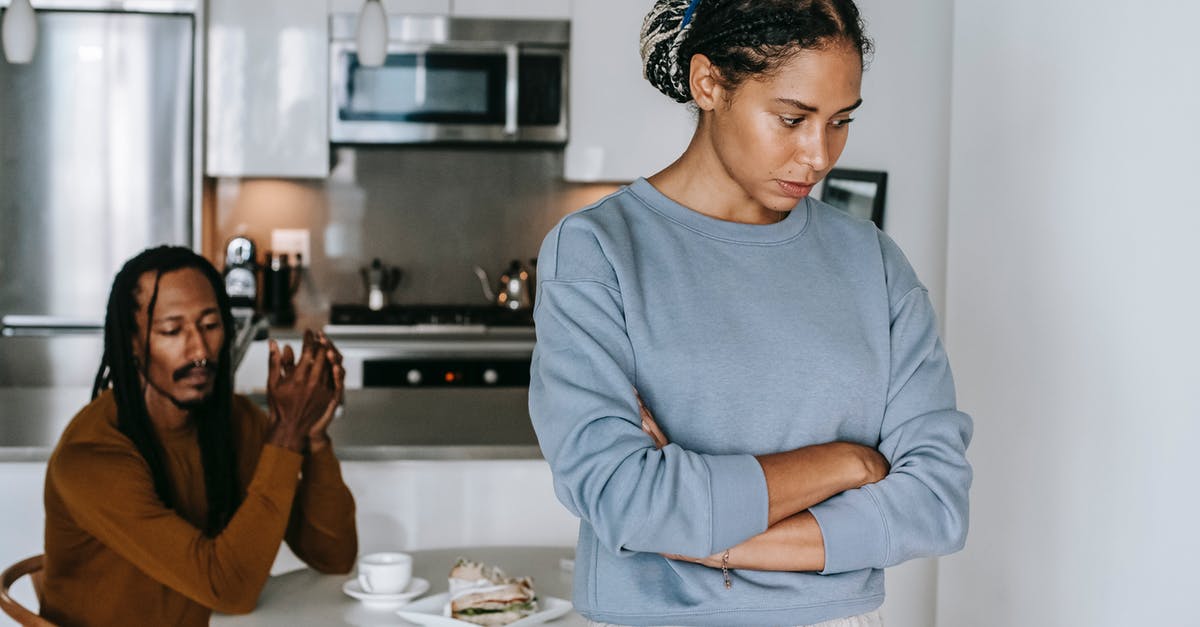 Dense and gluey centered cake problem - Young discontented African American female with folded arms against male partner at kitchen table during quarrel