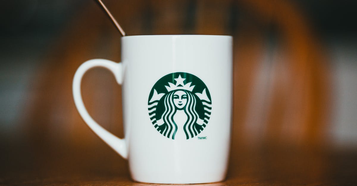 Describing the taste of Illy coffee and similar brands - Closeup of white ceramic mug with logotype of brand with hot drink and teaspoon placed on wooden table