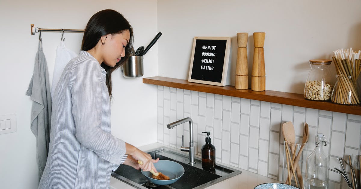 Detergent Contamination of Processed Foods - Side view of Asian female with brush washing dishes at sink while doing housework in light kitchen with supplies at home