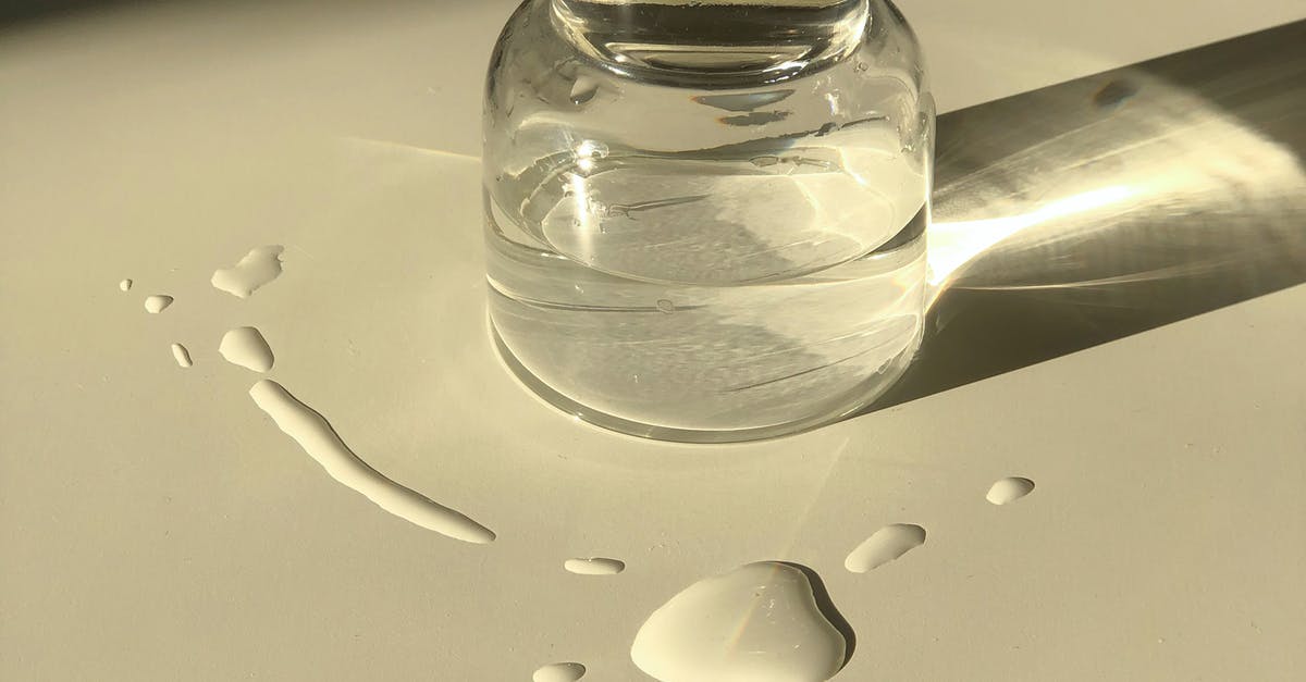 Device to install on a bottle to only spill drops - Glass jar with transparent liquid placed on white table