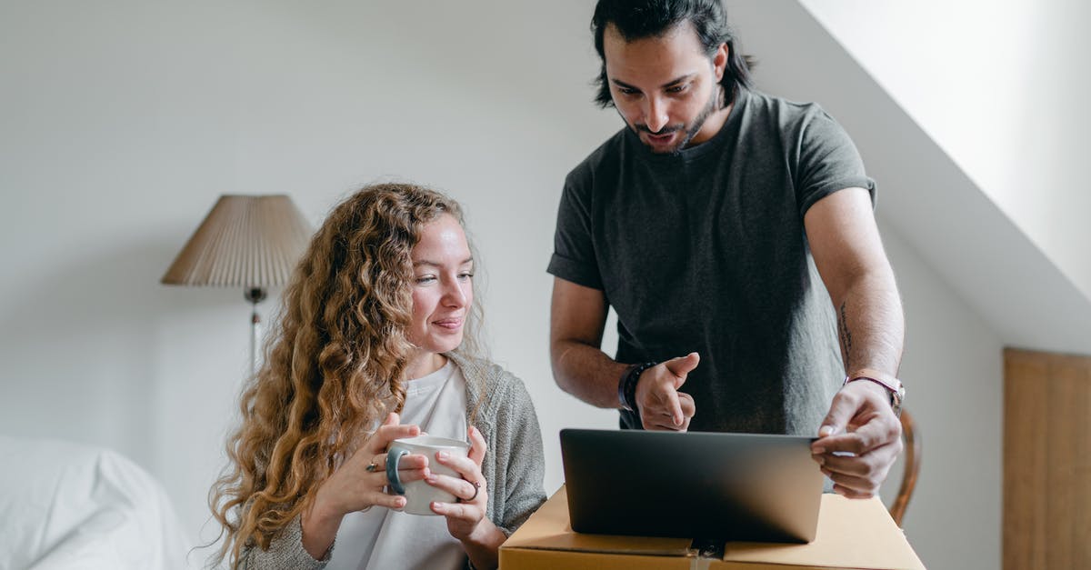 Device to squeeze last yogurt out of carton - Positive happy young couple in casual clothes packing belongings into carton box and using laptop in living room near window