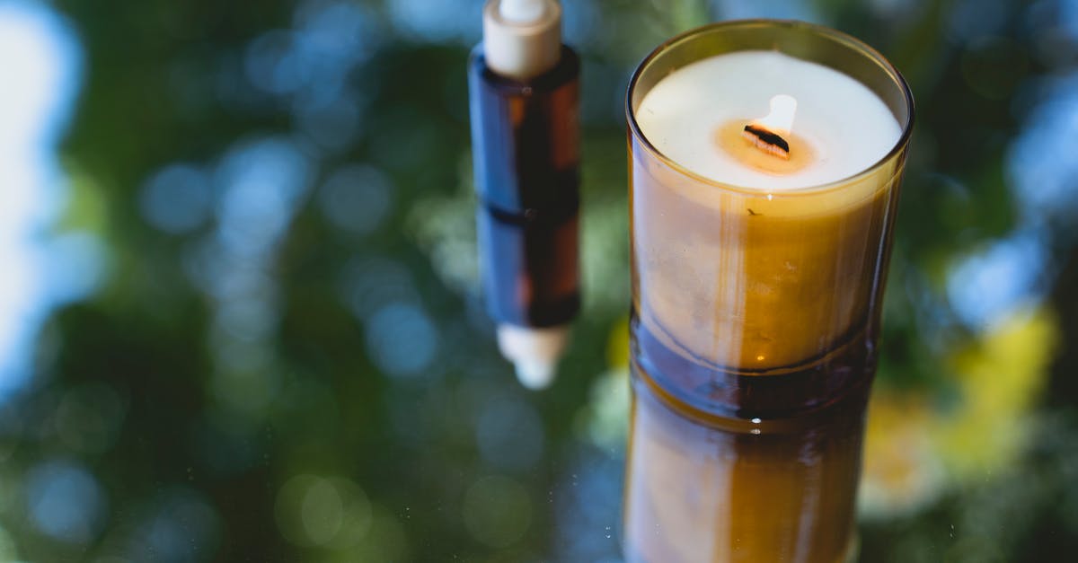 Did I just almost start an oil fire? - High angle of fragrant burning candle placed near amber glass bottle of essential oil on reflecting table