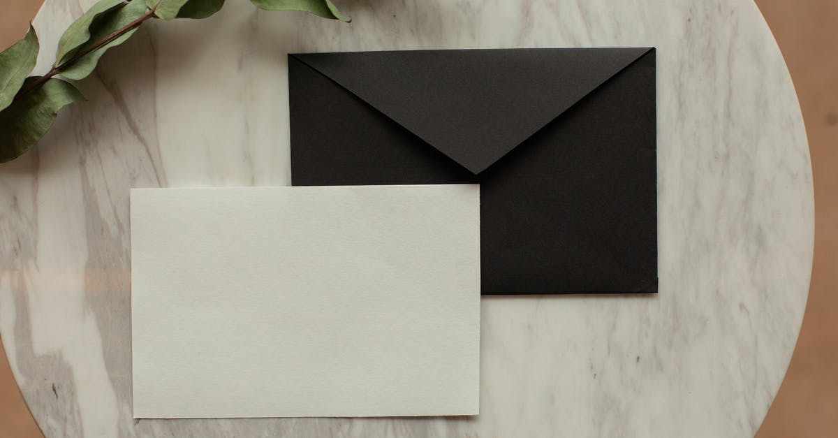 Difference between natural and organic - Top view of blank black envelope with white card placed on table with pencil and dry green sprig in modern room