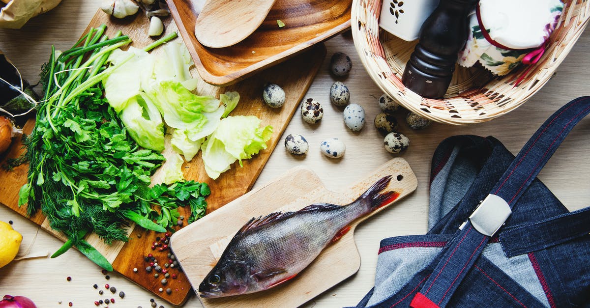 Difference between parsley and coriander(cilantro)? - Top view of fresh fish and vegetables put on cutting board near wooden dishware and wicker basket with pepper shaker and jar in kitchen