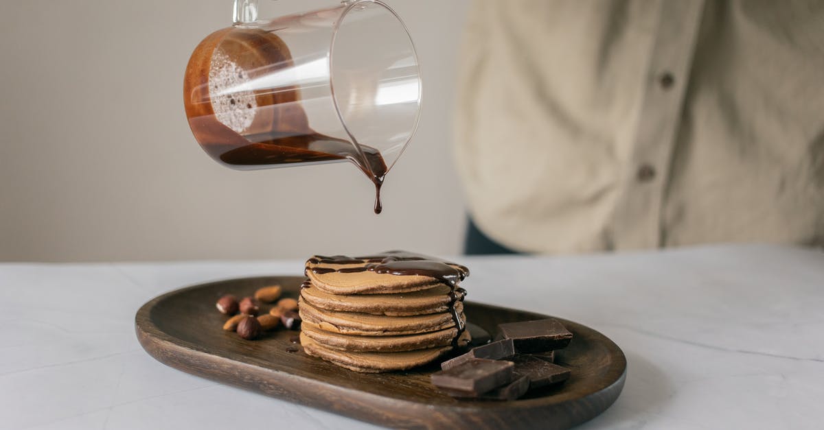 Difference between Potato Pancake and Hash Browns? - Crop anonymous person pouring fresh chocolate from jug on appetizing pancakes placed on timber board on table